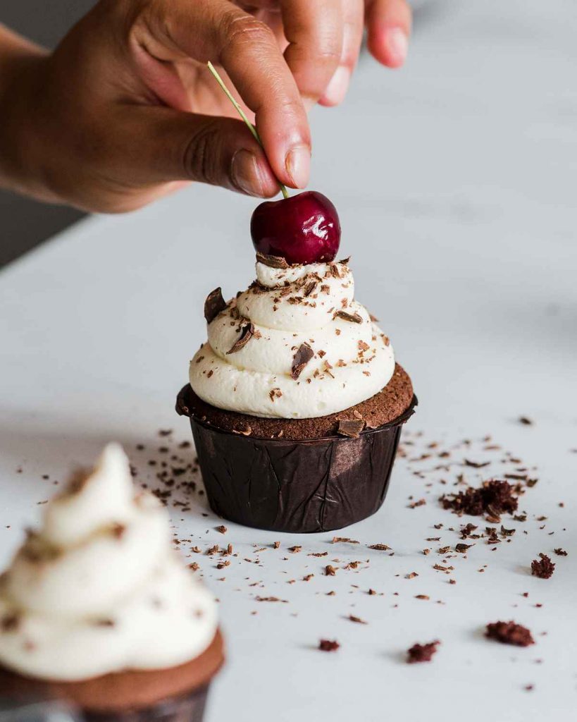 Adding the final touch: the cherry on top of the Black Forest cupcake! Recipe by movers and bakers