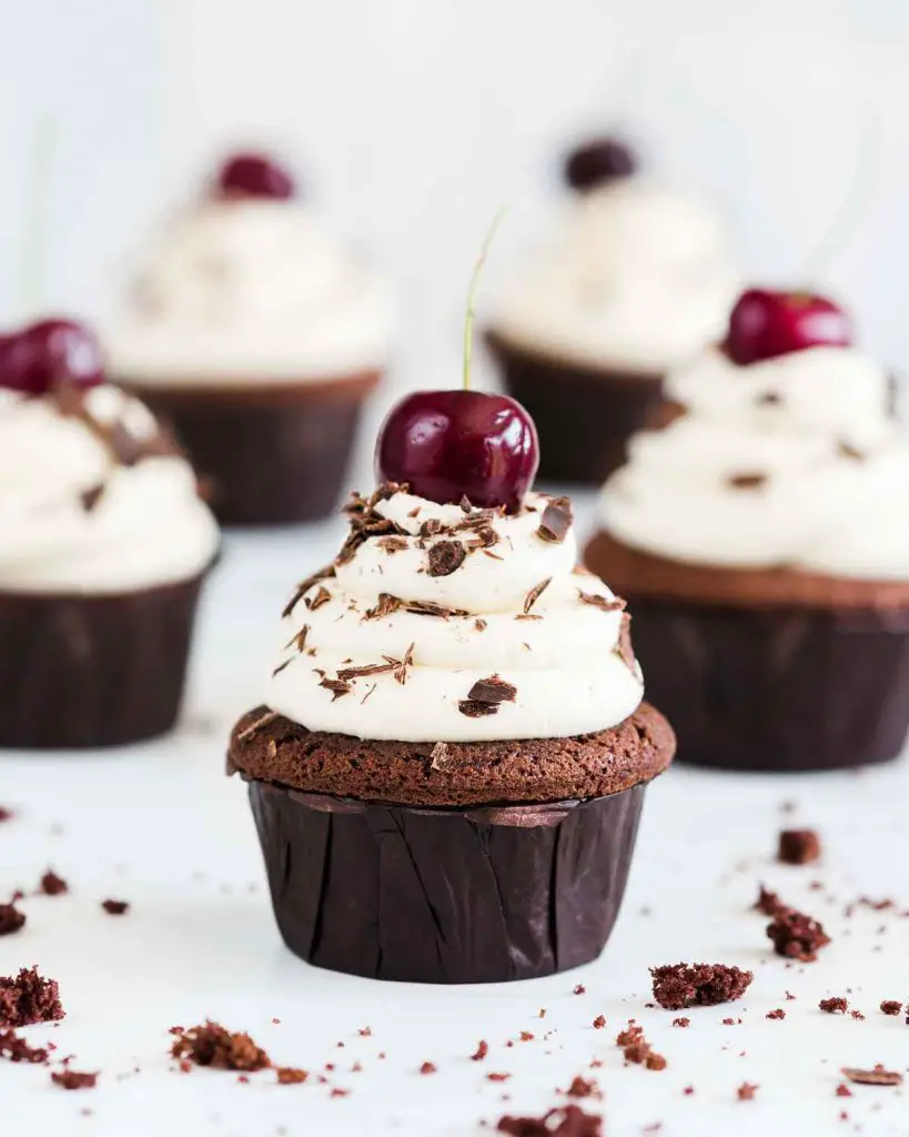 My Black Forest cupcakes are light but deeply chocolatey cupcakes, laced with Kirsch and filled with delicious black cherry compote, then topped with a buttercream swirl, grated chocolate and a cherry on top. Recipe by movers and bakers