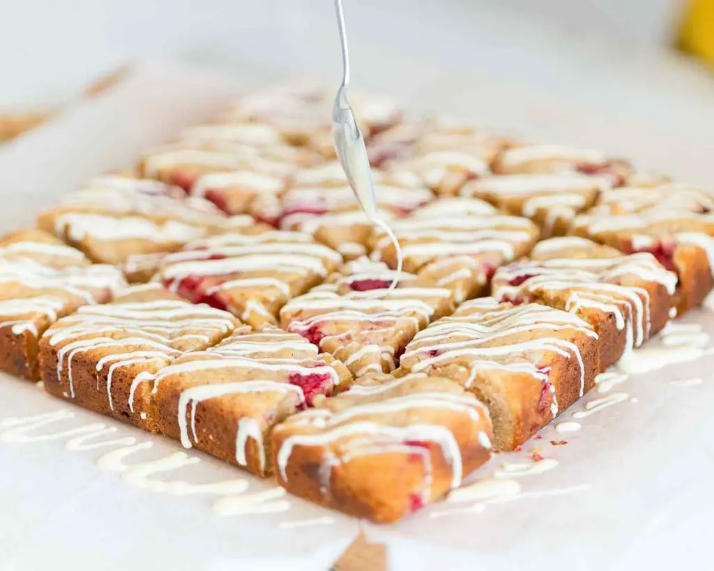 Adding the finishing touch of white chocolate drizzle over the raspberry blondies. Recipe by movers and bakers