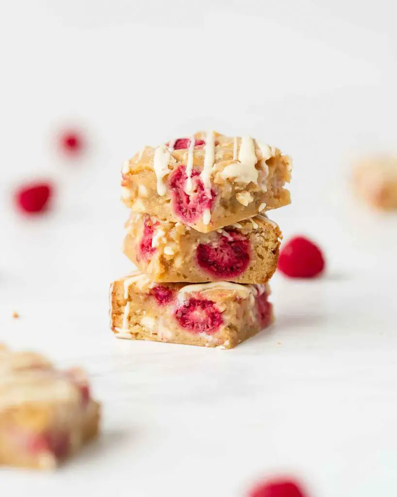 A stack of three raspberry white chocolate blondies. Recipe by movers and bakers