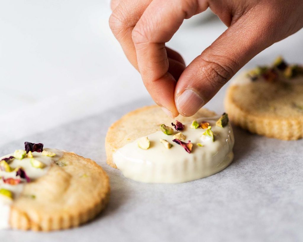 Adding finishing touches by sprinkling on dried rose petals and chopped pistachio onto the shortbread for decoration