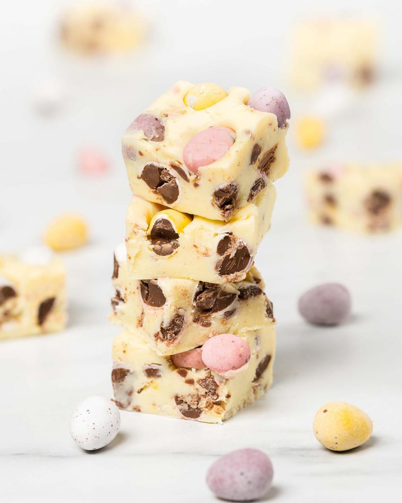 A stack of mini egg fudge pieces. A soft and creamy quick fudge recipe packed with lots of delicious mini eggs! Recipe by movers and bakers