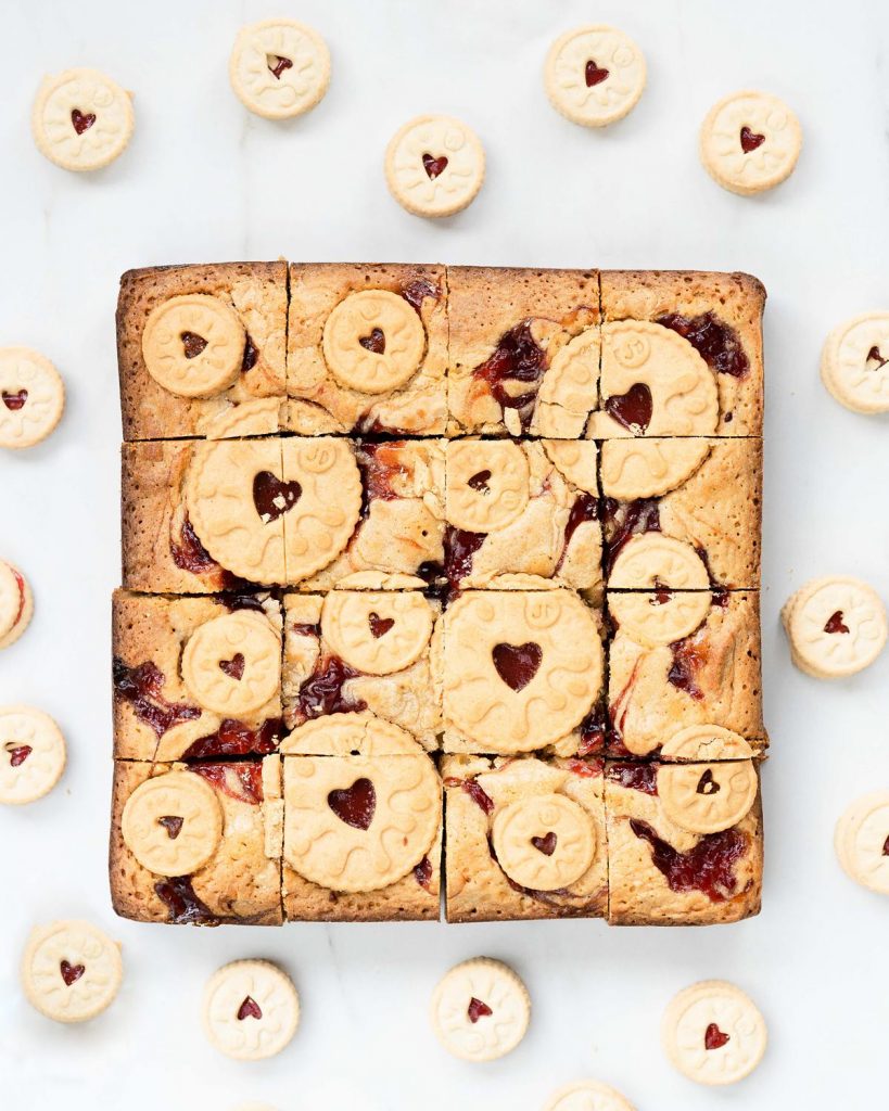 Jammie dodger blondies. Yummy fudgy white chocolate blondies packed with beautiful jammie dodger biscuits and swirls of smooth raspberry jam. Recipe by movers and bakers