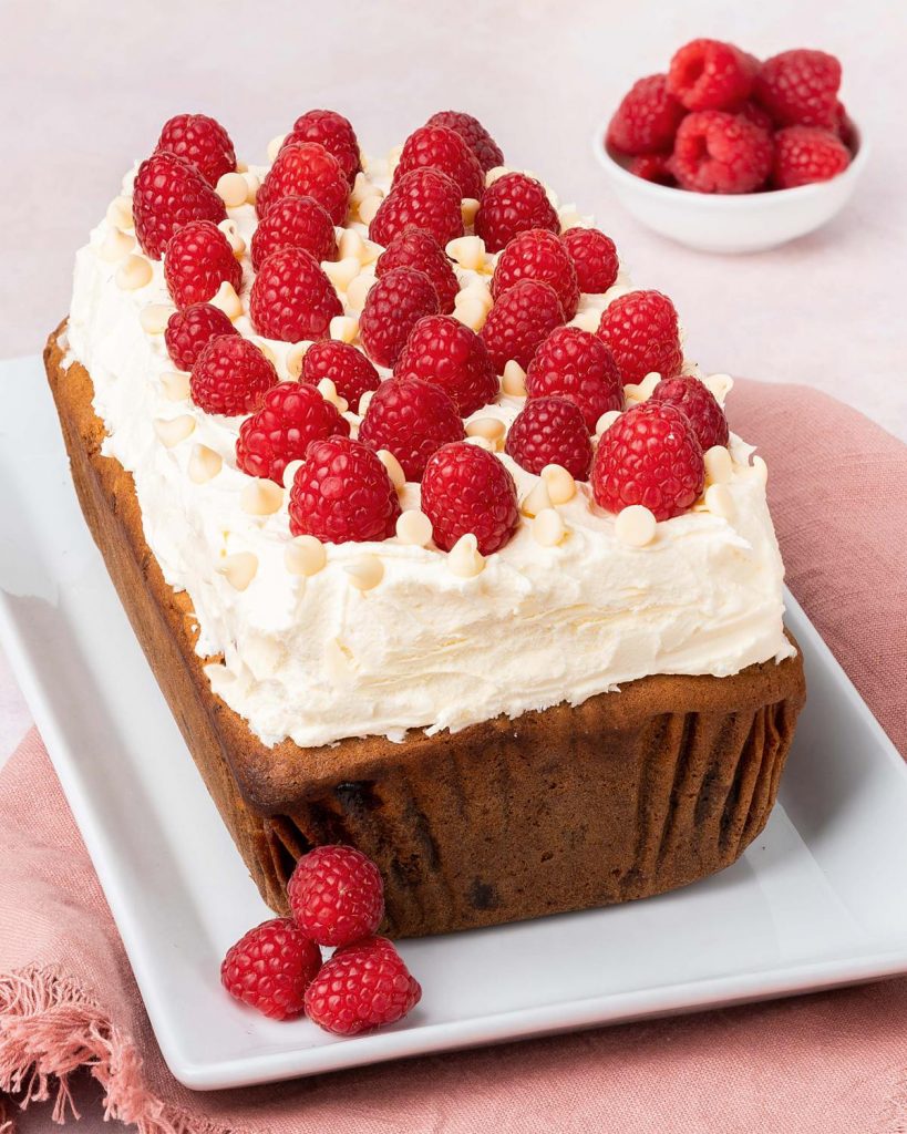 Raspberry and white chocolate loaf cake. A beautiful loaf cake packed with fresh tart raspberries and sweet white chocolate chips, topped with a white chocolate buttercream and more fresh raspberries. Recipe by movers and bakers