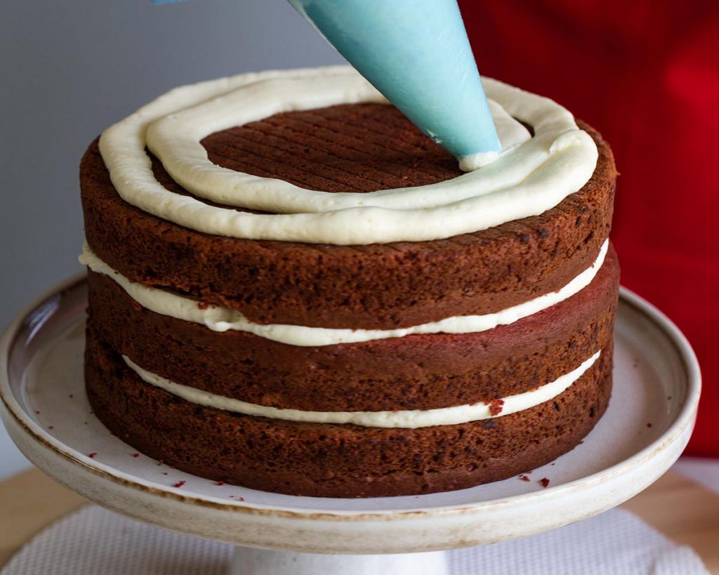 Piping icing on each cake helps ensure an even spread of icing between each layer and around the sides of the cake. Recipe by movers and bakers