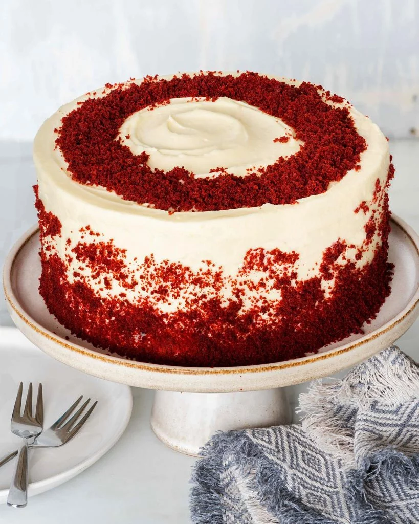The best eggless red velvet cake recipe. Delicious light chocolate and vanilla flavoured cake layers filled and covered with a beautiful rich cream cheese icing then decorated with red velvet cake crumbs. Recipe by movers and bakers