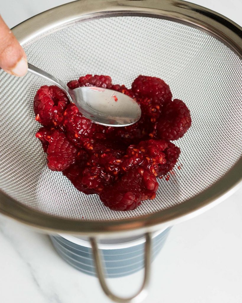 Pressing the fresh raspberries through a sieve to extract the juice without the seeds or pulp. Recipe by movers and bakers