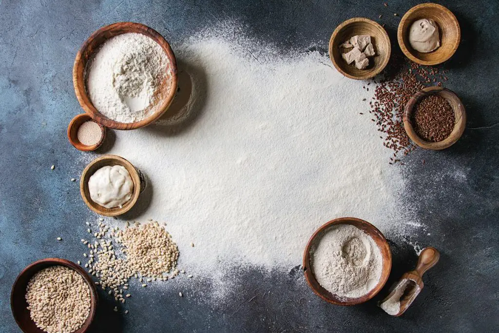 flour conversions. Ingredients for baking bread. Variety of wheat and rye flour, grains, yeast, sourdough and sifted flour over dark blue texture background.