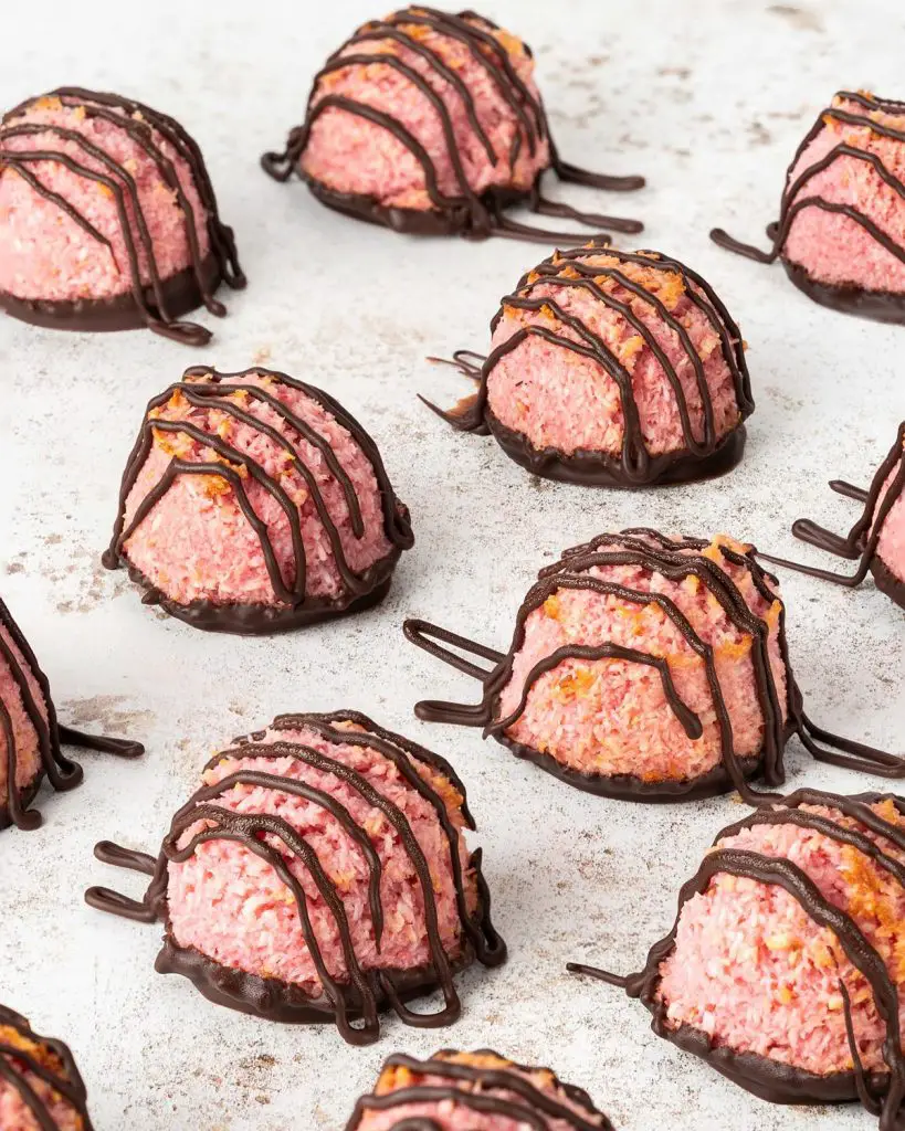 Finished raspberry macaroons are drizzled in dark chocolate before being left to set. Recipe by movers and bakers