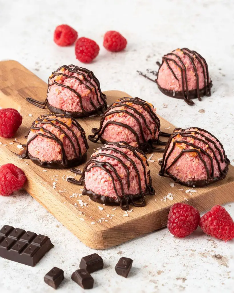 Raspberry chocolate macaroons served on a wooden board with added raspberries and dark chocolate pieces in the image. Recipe by movers and bakers