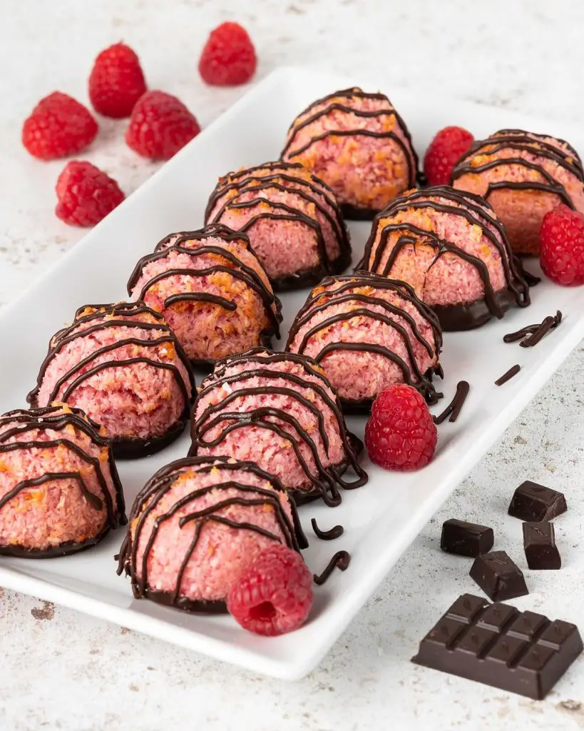 Raspberry chocolate macaroons placed on a plate with dark chocolate chunks and fresh raspberries. Recipe by movers and bakers